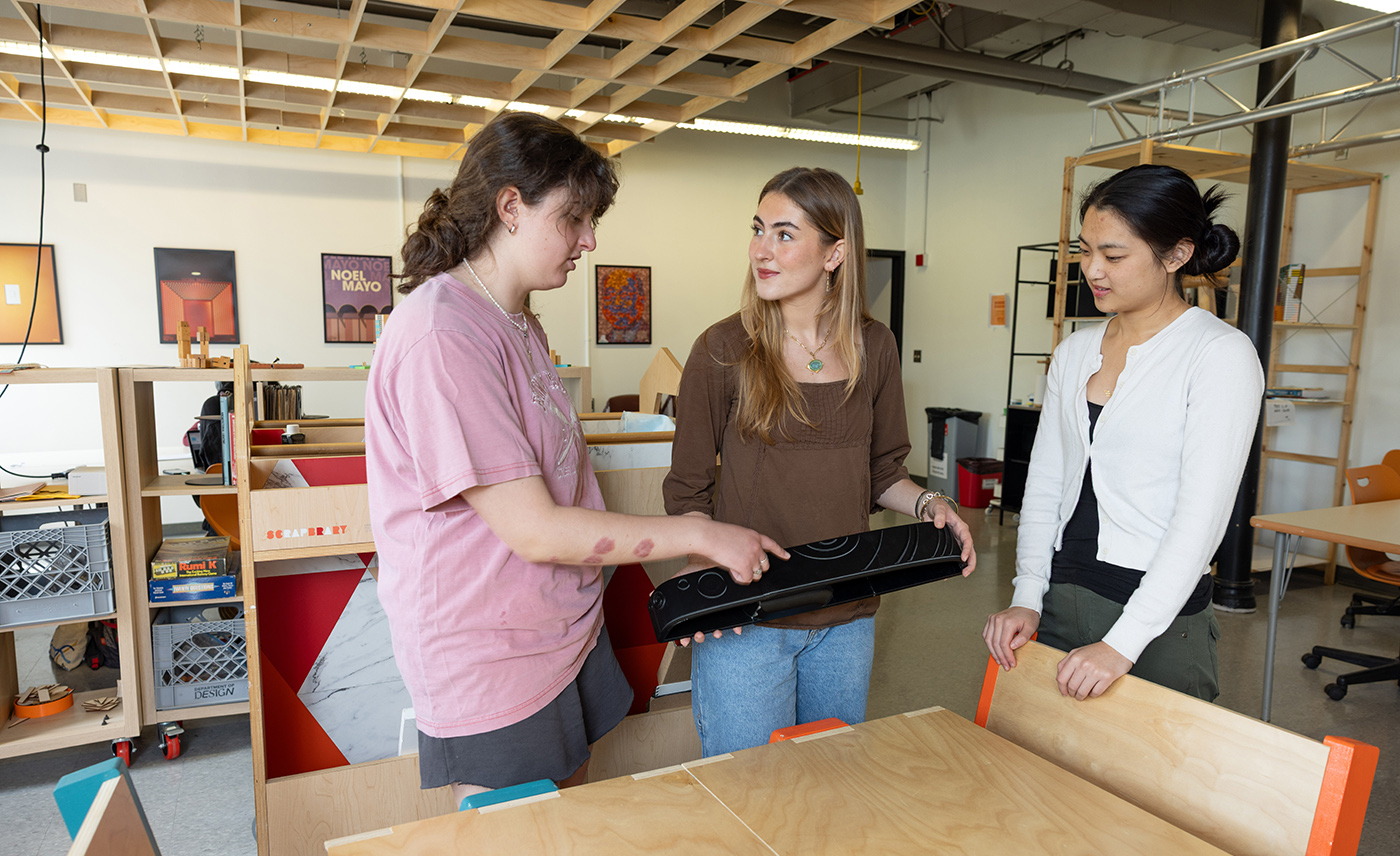 Three students stand together in a lab and examine a 3D-printed tactile armrest panel