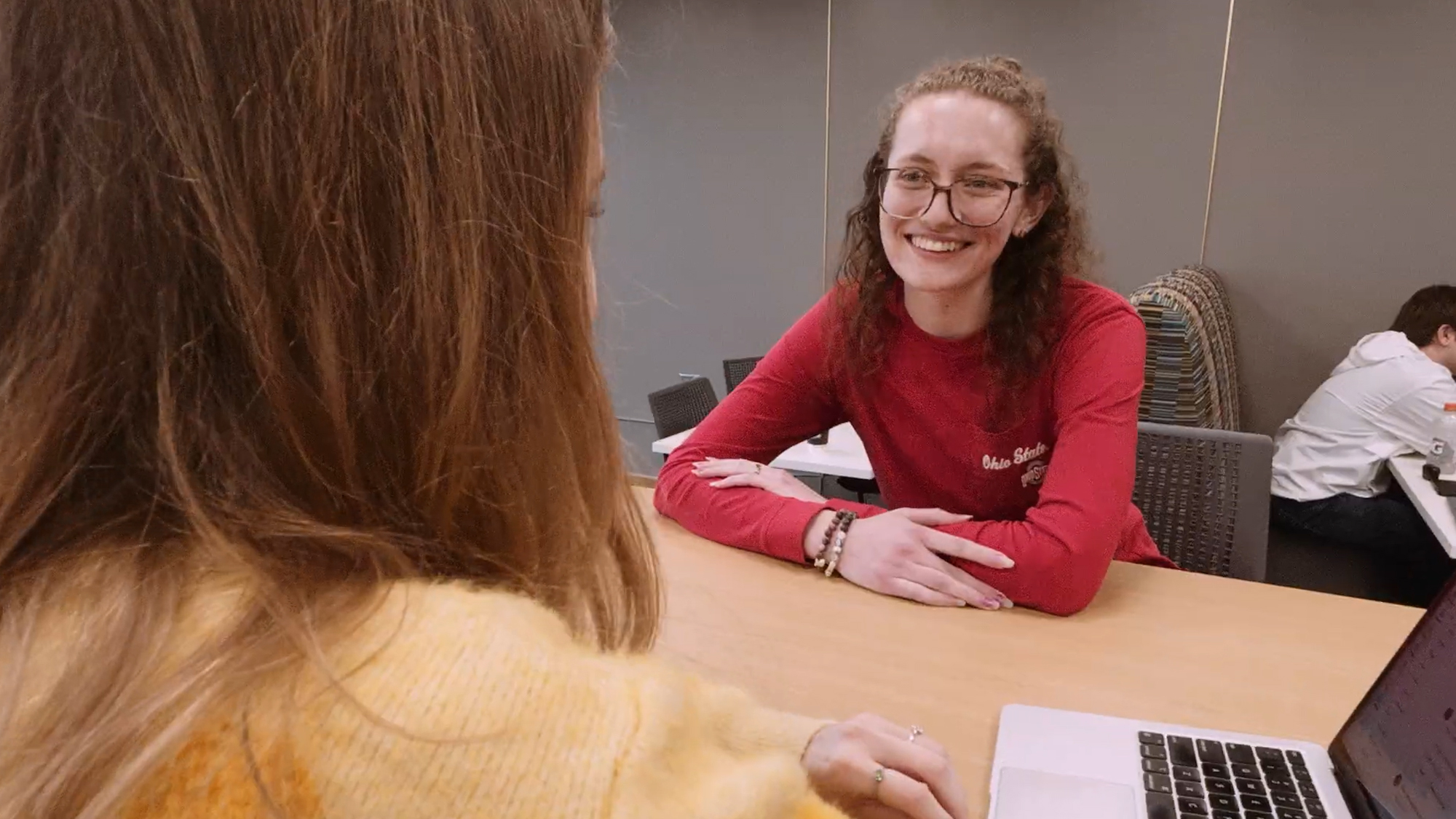 A woman sitting at a desk smiles at a woman sitting across from her.