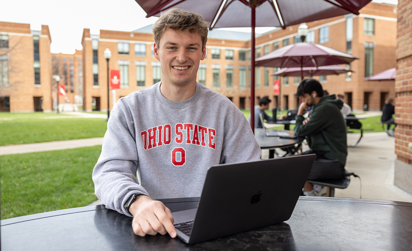 A student sits at a table with a laptop in front of him on the Fisher College of Business campus at Ohio State