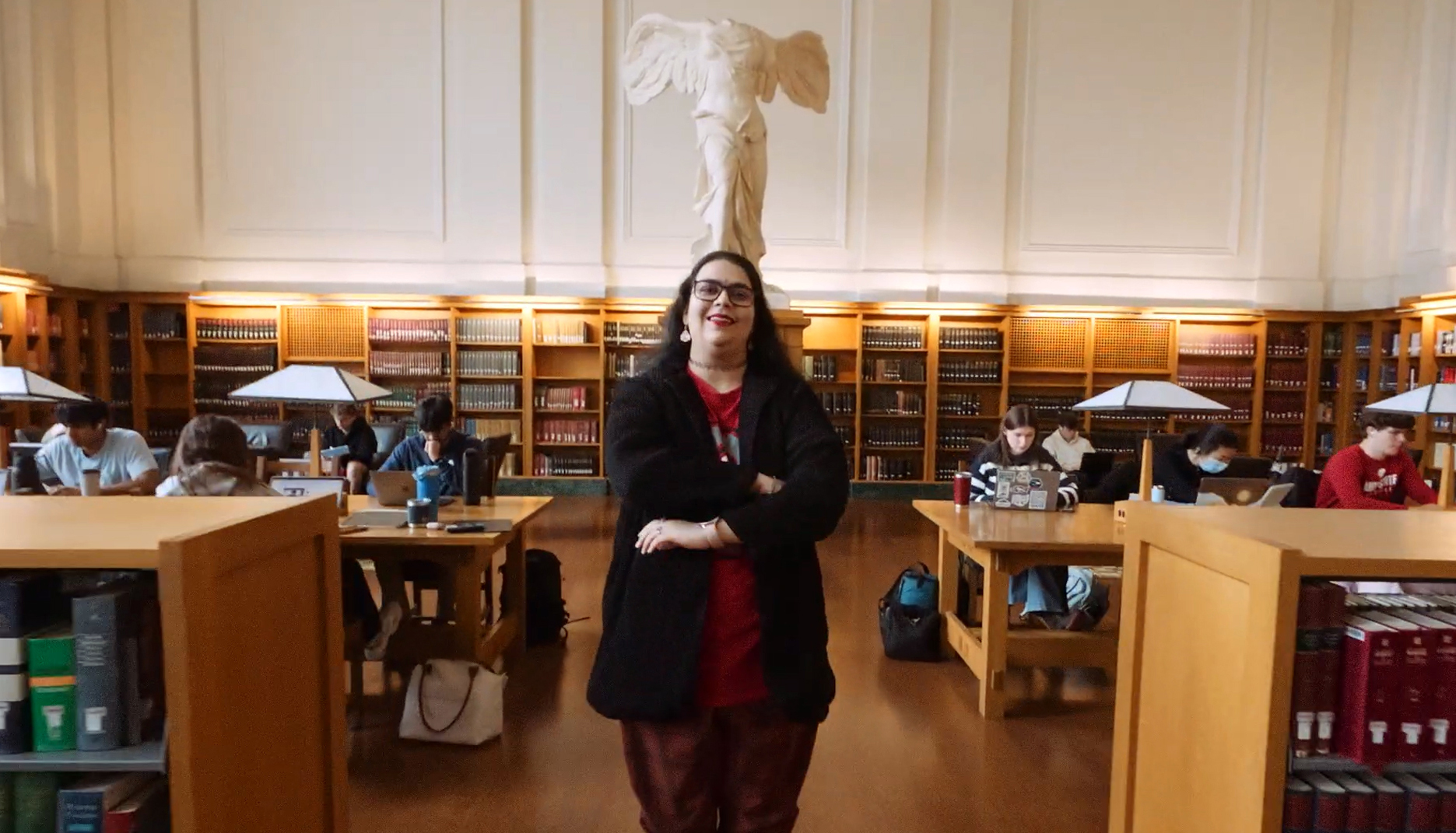 A young woman stands with her arms folded in the grand reading room of Ohio State's Thompson Library.