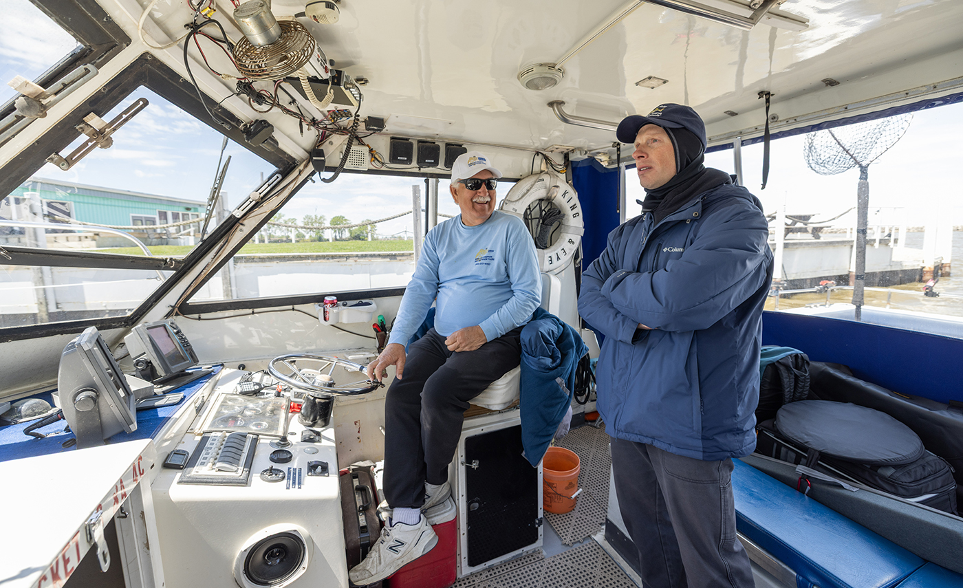Two men stand in the helm of a boat and talk