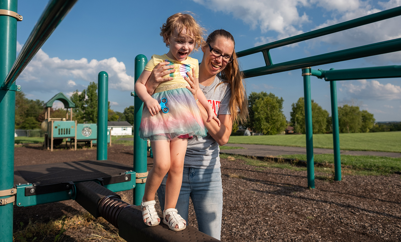 A mother holds her daughter as she walks across a balance beam on a playground