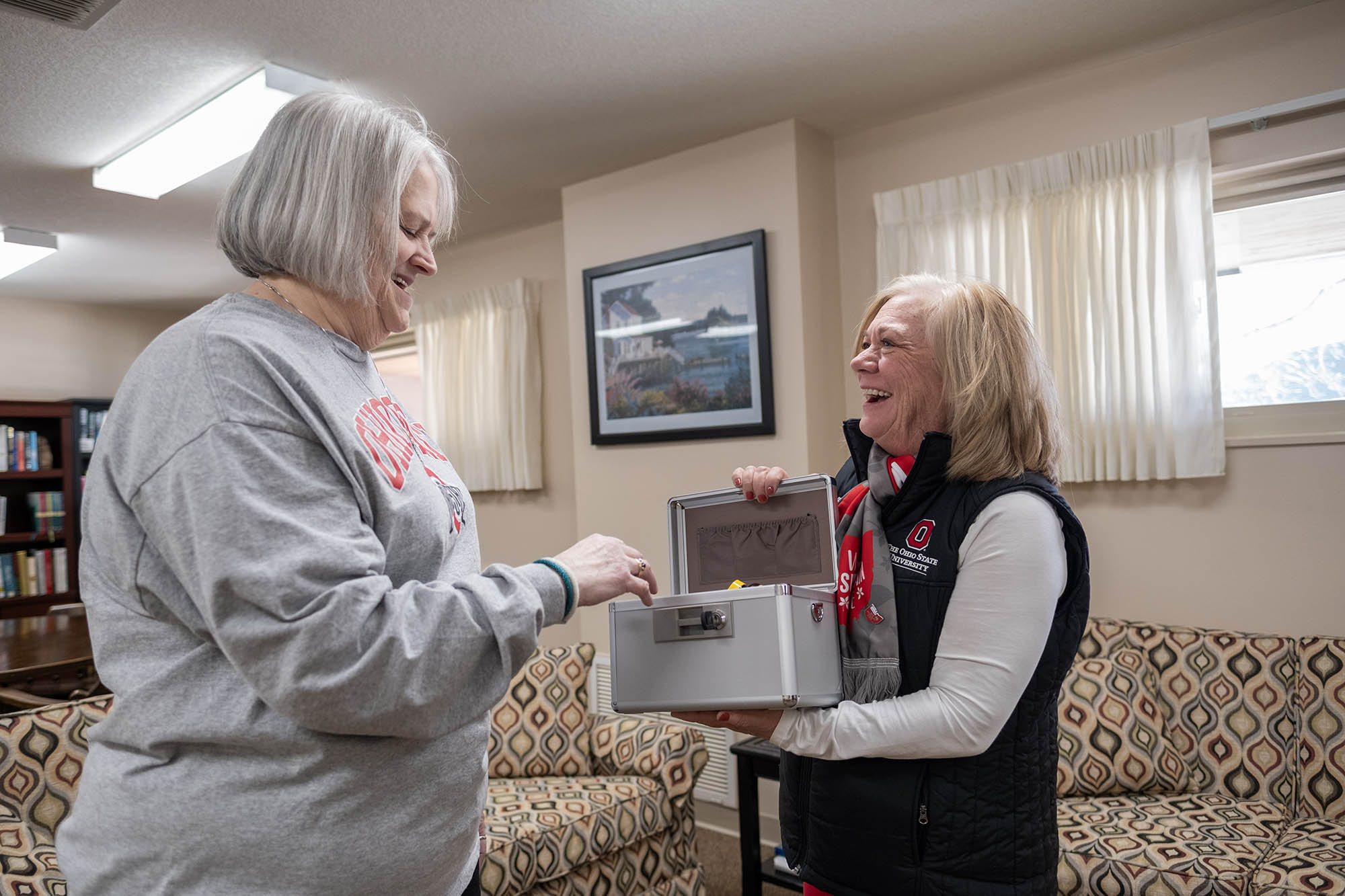 A woman opens a box that another woman is holding.