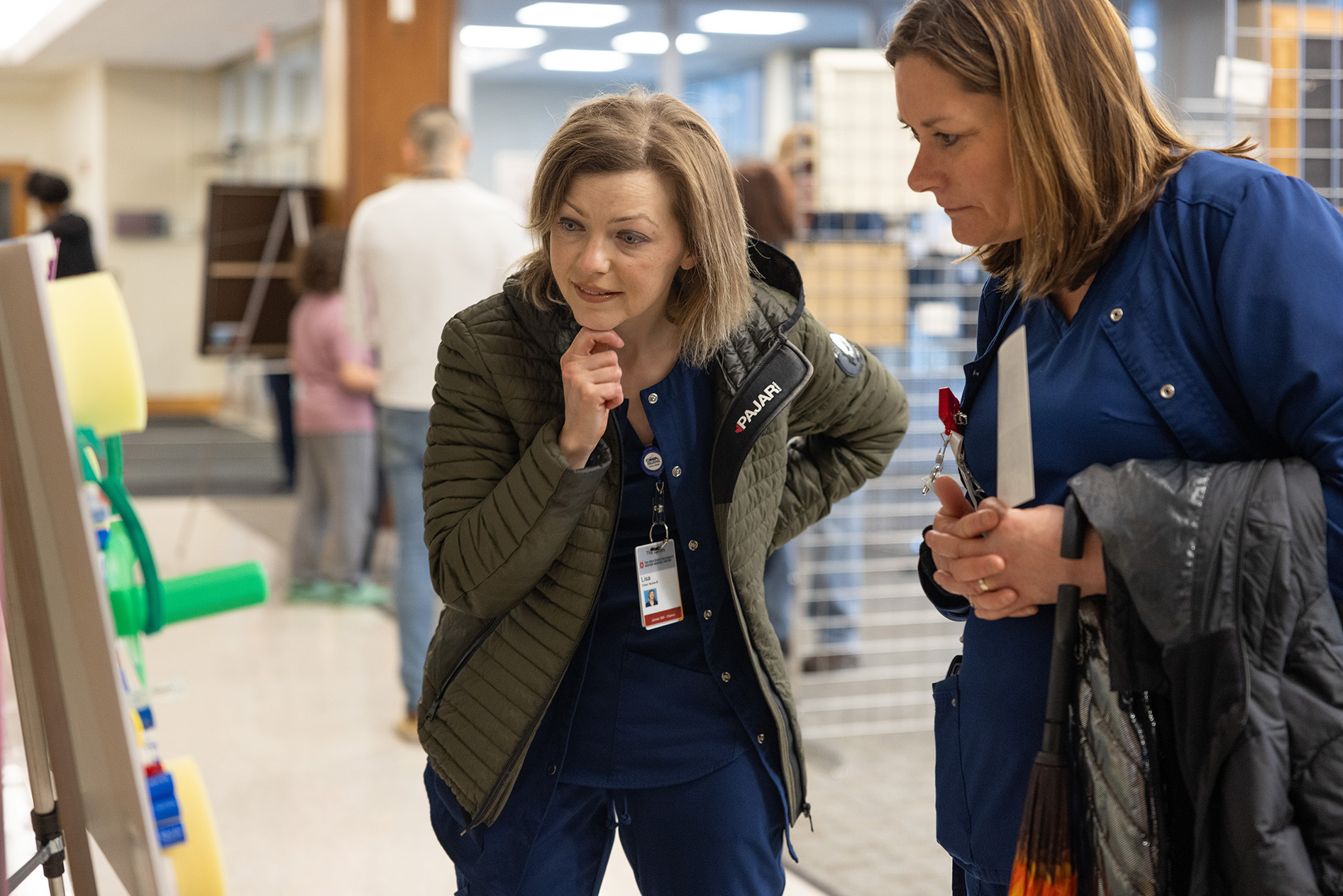 Two women in nursing scrubs bending over to examine framed art