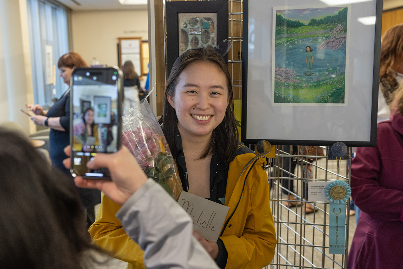 Michelle Huynh smiling with a bouquet of flowers in front of her artwork getting her photo taken