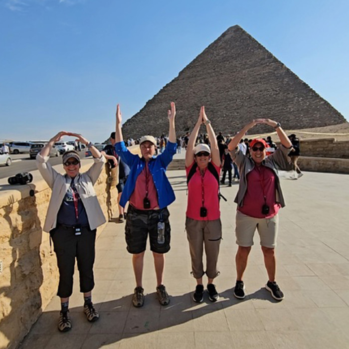 A group of four people spell OHIO in front of an Egyptian pyramid 