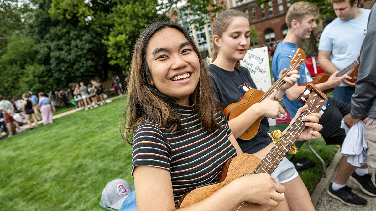A student playing the guitar on the Oval smiles at the camera during Ohio State's annual involvement fair