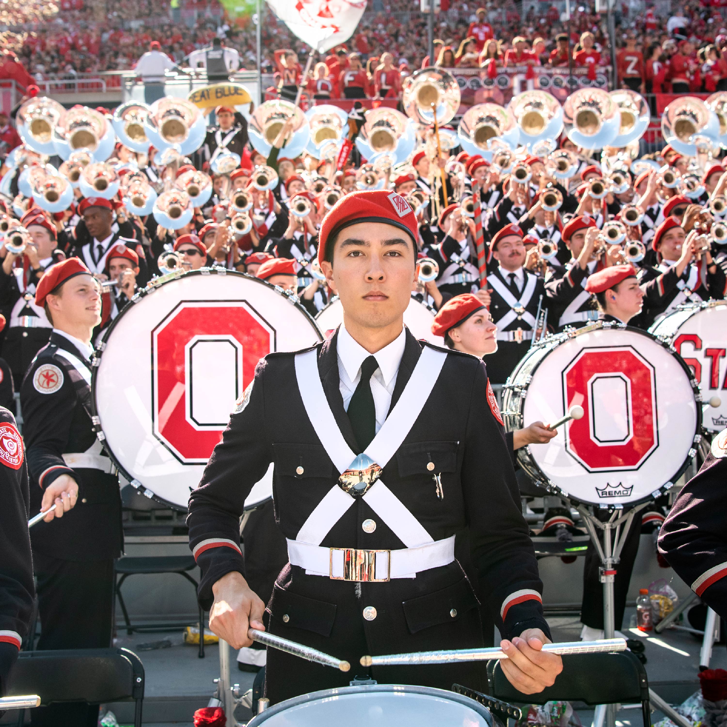 A drummer in the Ohio State Marching Band holds his beat and is flanked by two bass drummers with sousaphone players in the background