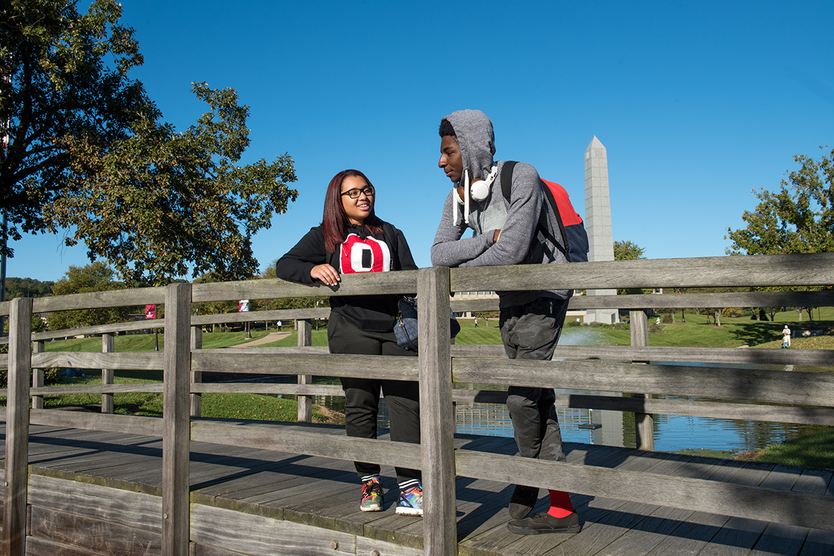 Two students standing on a bridge talking on the Newark campus