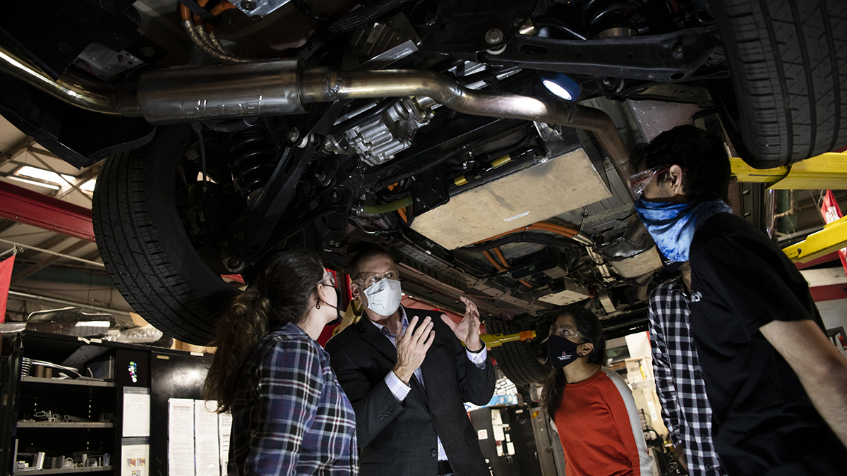 Shawn Midlam-Mohler talking to students while a car is suspended overhead