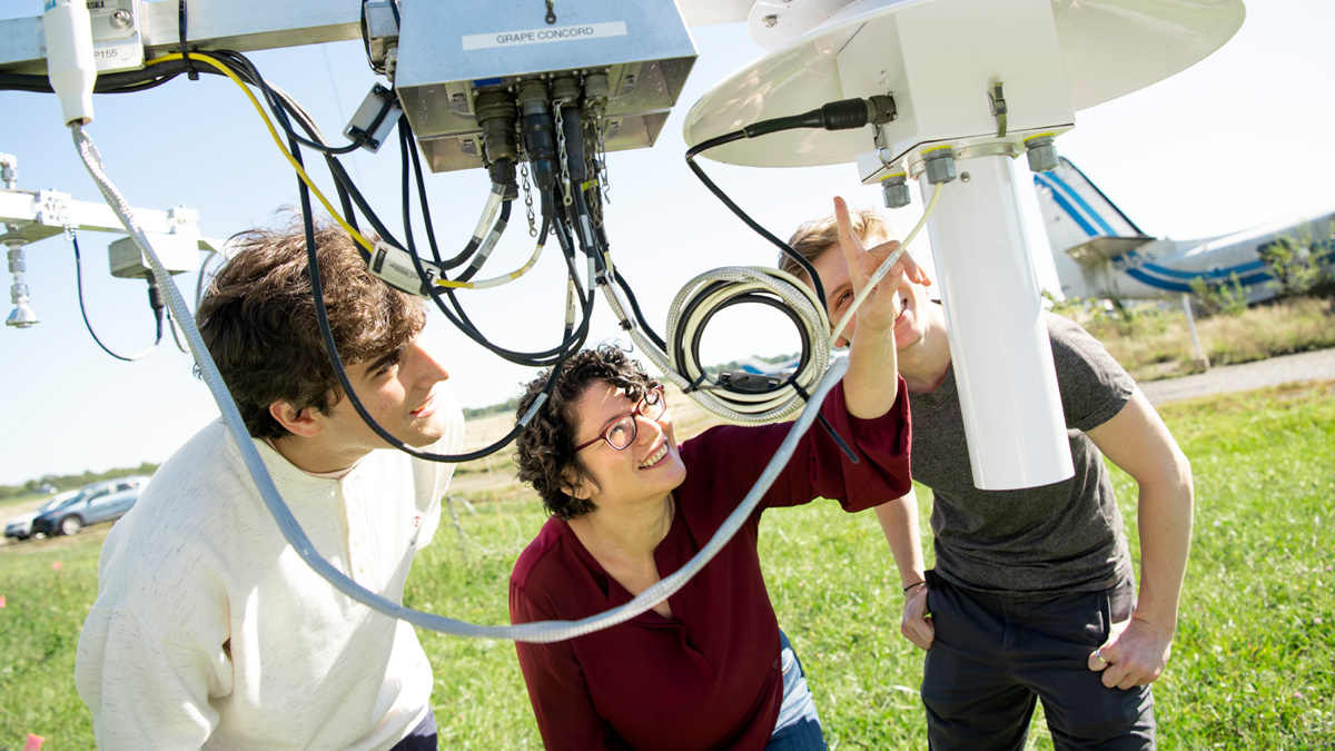 Tanya Berger-Wolf (middle), director of Ohio State’s Translational Data Analytics Institute, and undergrad students in her research lab, Cameron Erdman (left) and Craig Fouts, look at sensors on a tower at the Ohio State Airport.