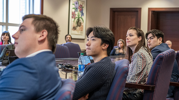 Students sitting at a large table while focused on information being presented