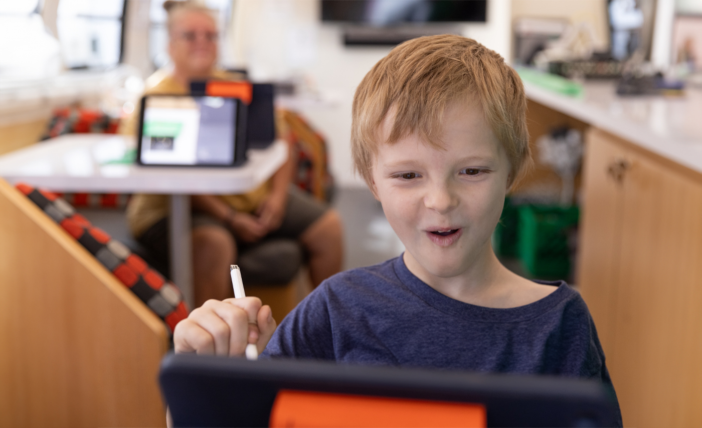 A boy smiles as he uses an iPad.