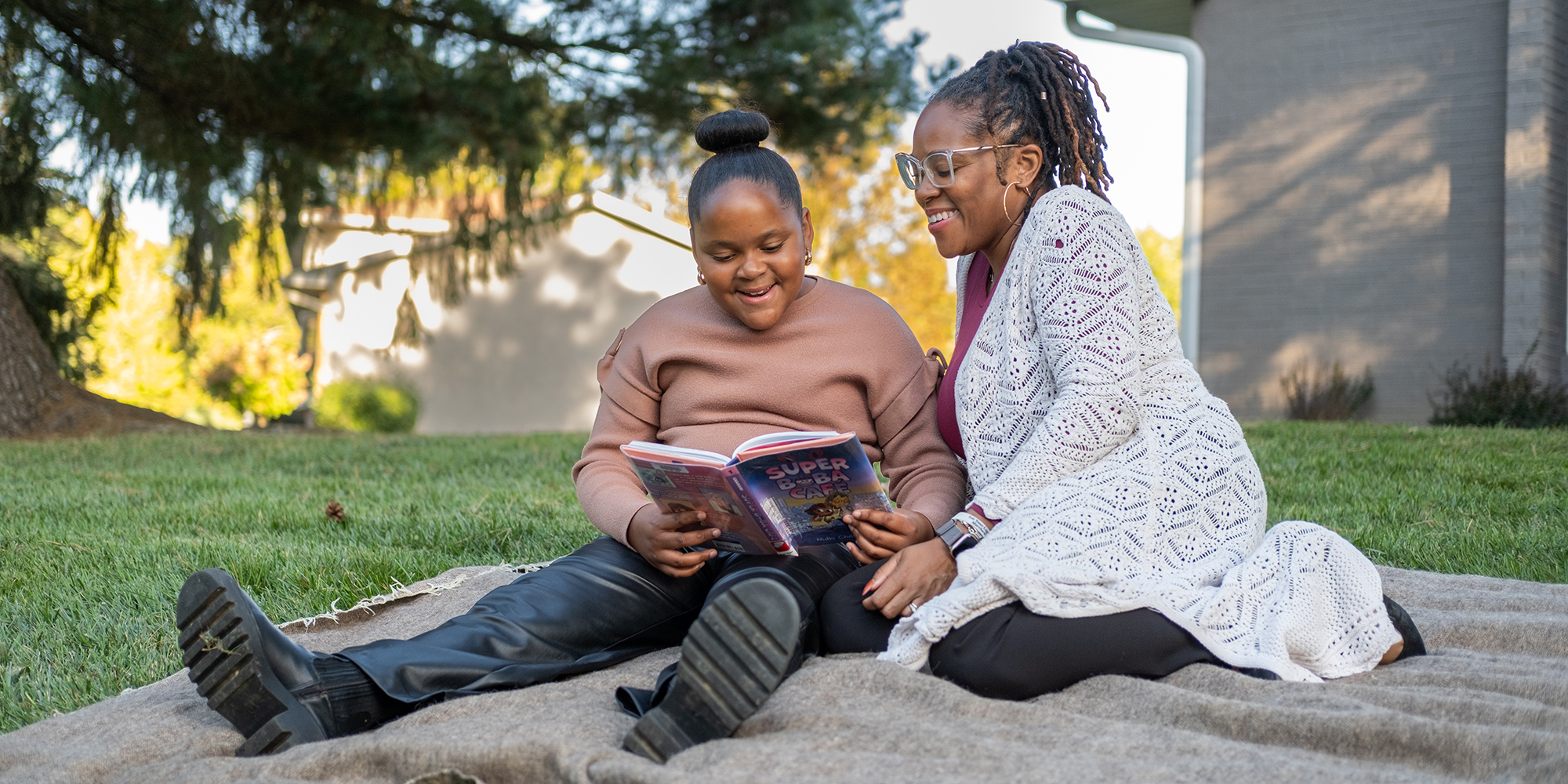A mother and her daughter sit together and read on a lawn