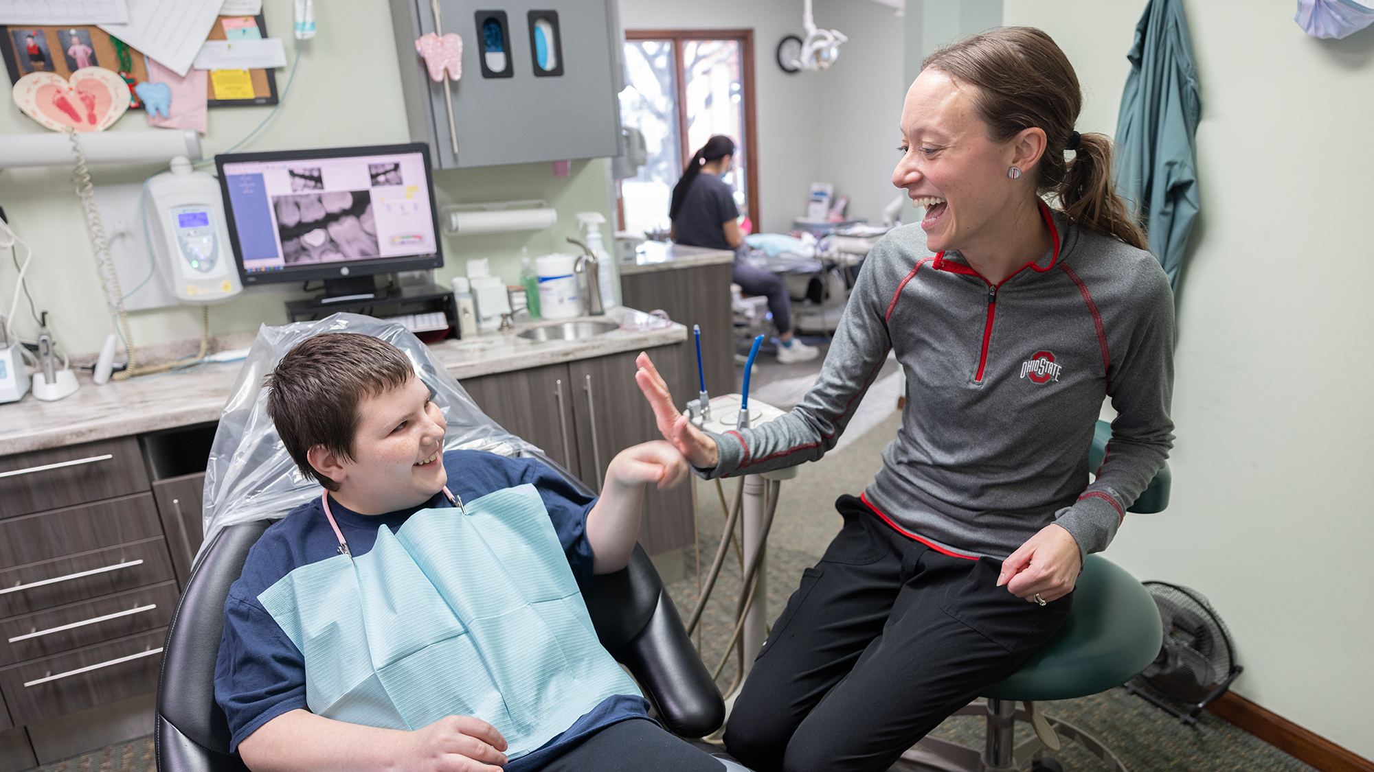A boy in a dentist's chair gives a fist bump to a dentist who is standing to his right.