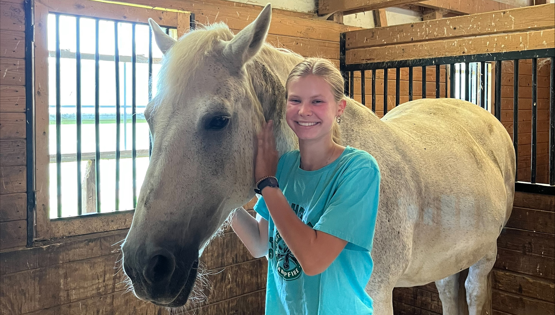 An Ohio State student stands with a horse in a stable.