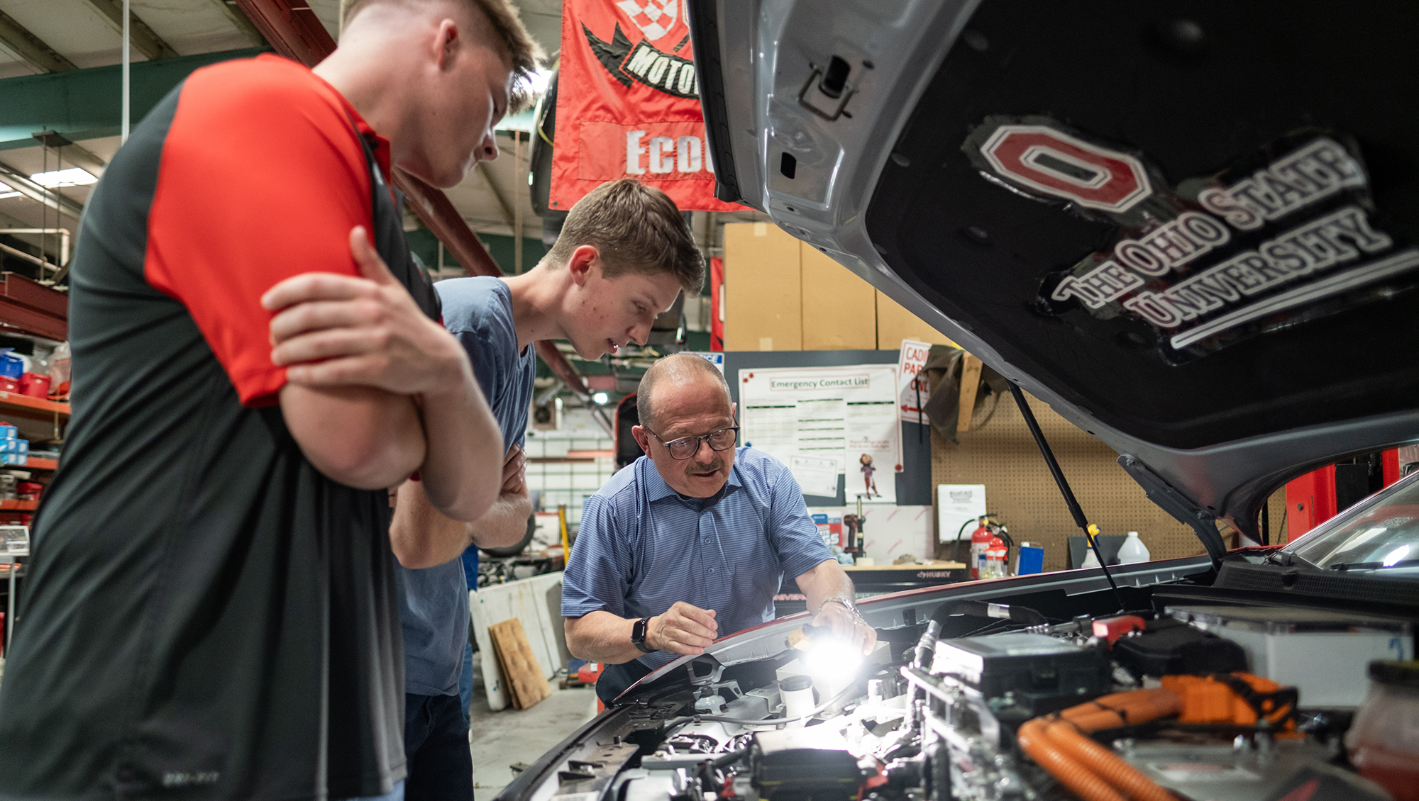 Giorgio Rizzoni and two student lean under the hood of a car and examine its engine.