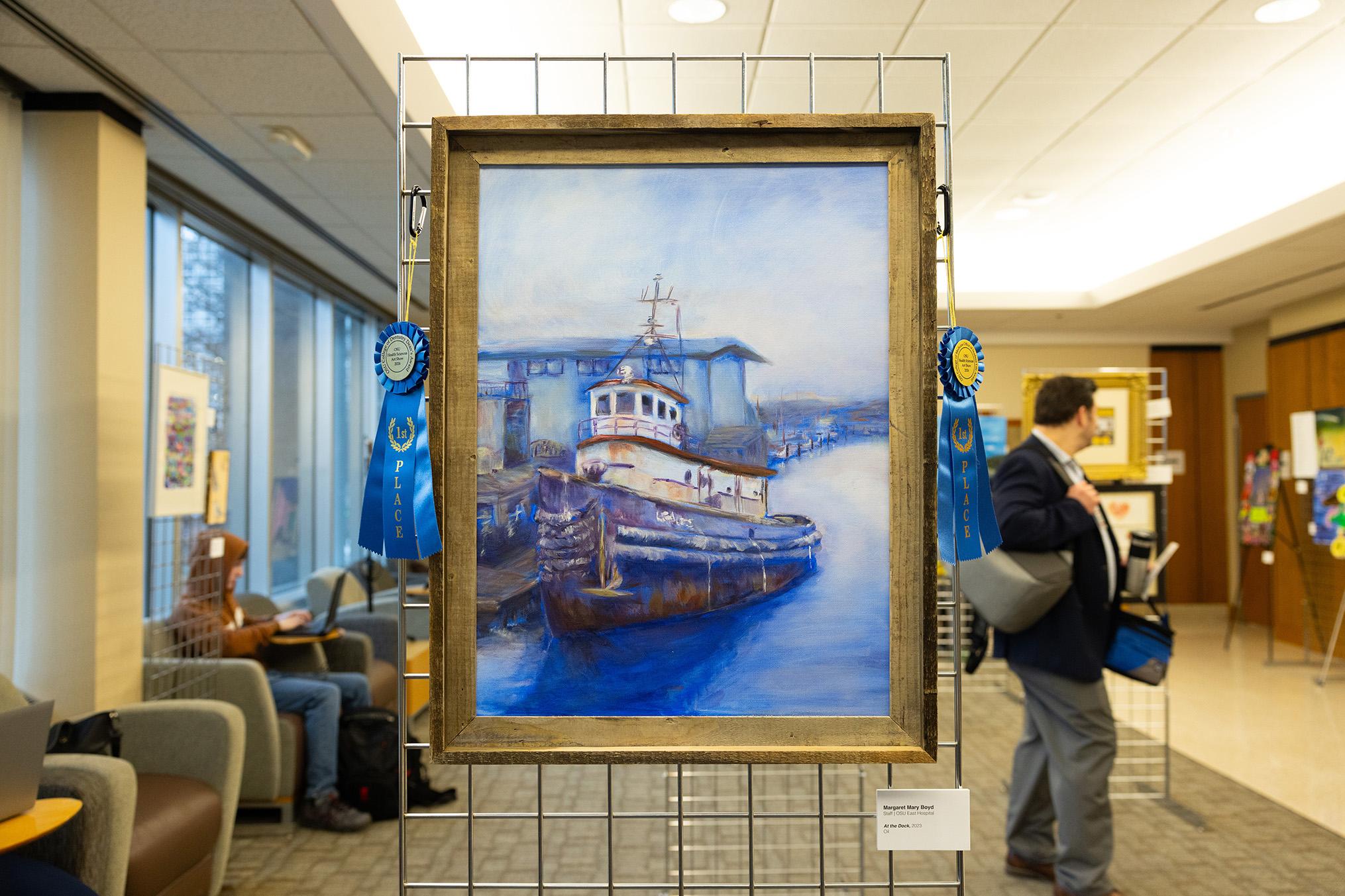 Painting of a ship at harbor in a gold frame with two blue ribbons