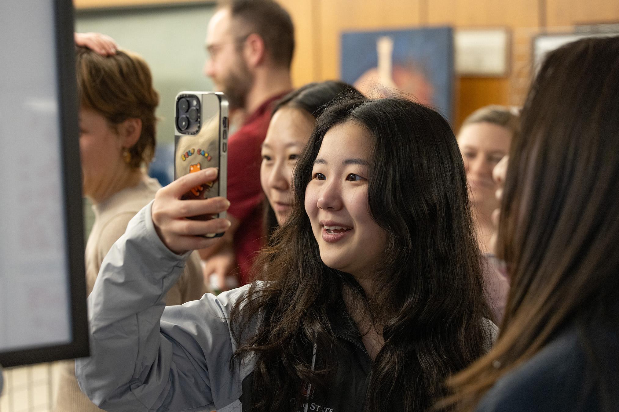 Woman in a crowd of people taking a photo of a piece of art