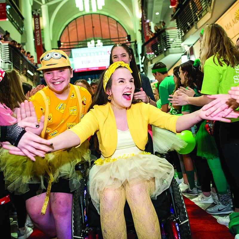 A girl in a wheelchair and another young person are high-fived by students during Ohio State’s BuckeyeThon cancer fundraiser
