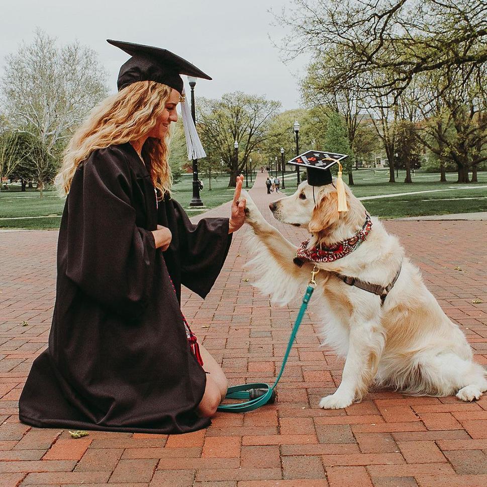 An Ohio State student in a cap and gown give a high five to a dog that’s wearing a graduates cap.