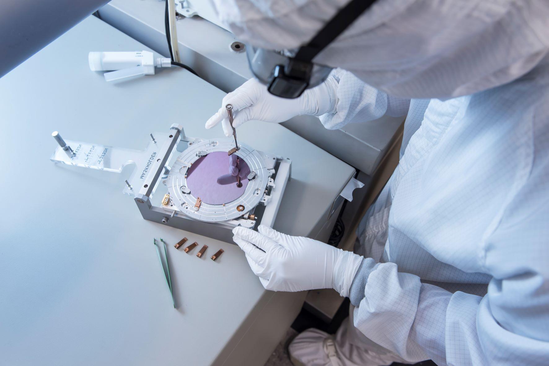 Person in full lab gear and gloves handling small delicate machinery