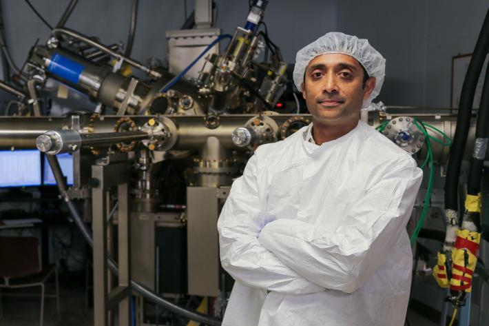 Rajan wearing sterile lab gear in front of complex machinery