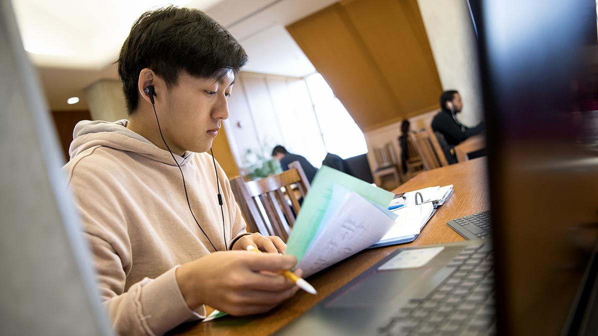 A student wearing headphones studies in the library