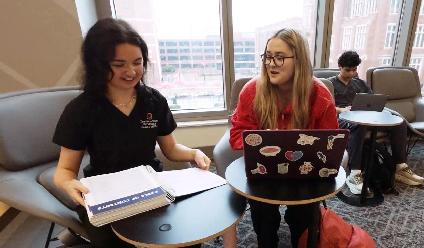 Two women sit at a table in a classroom setting.