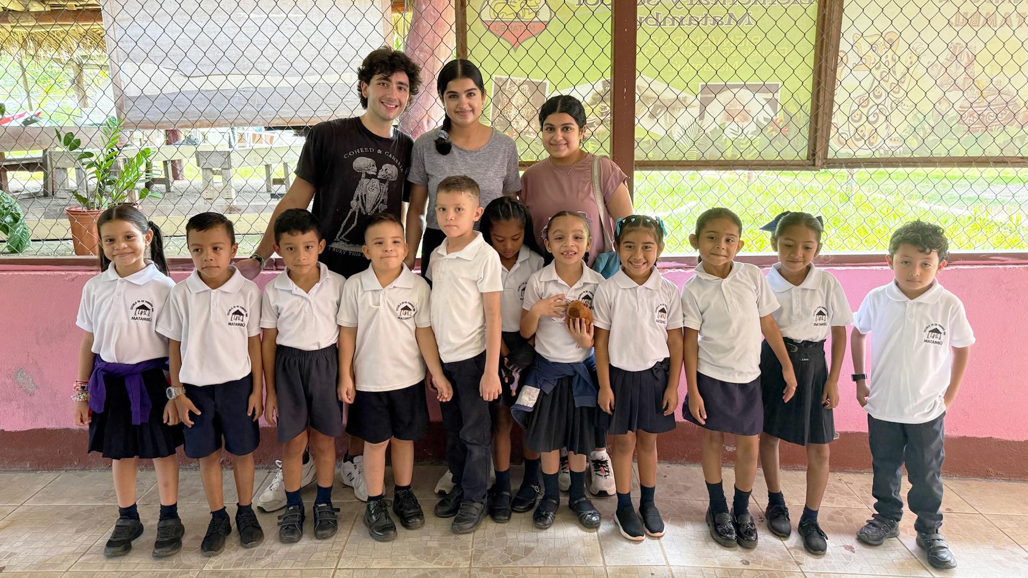 Three college students stand behind a row of children