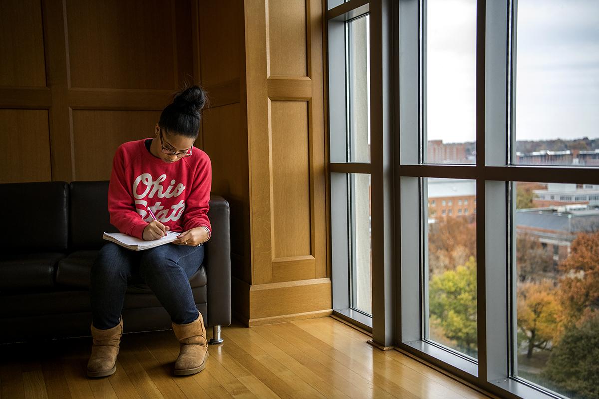 A student sits next to a large window while studying