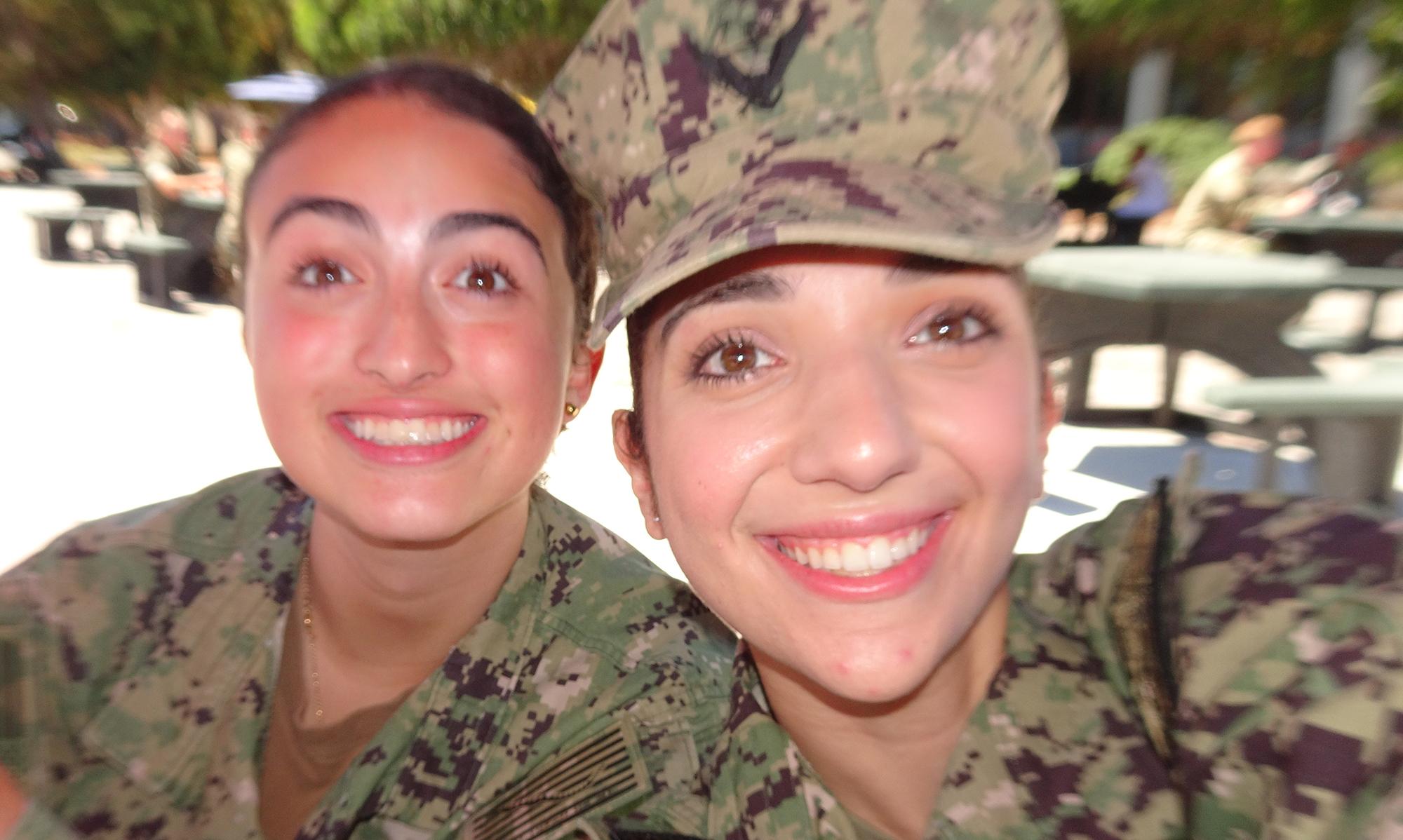 Two women in military fatigues smile and pose for the camera